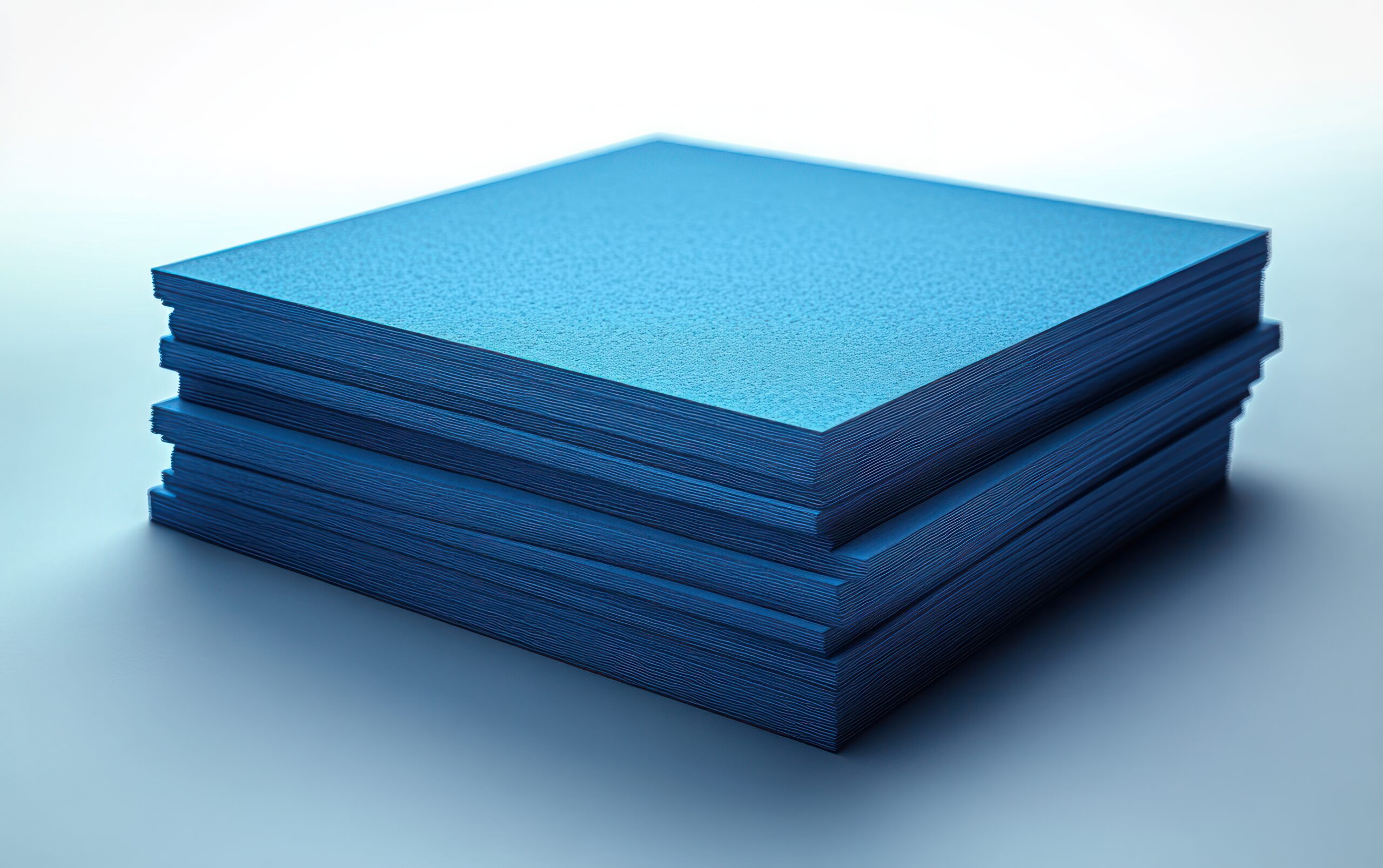 Stack of blue paper sheets neatly stacked on a reflective surface, with textured edges visible on the sides.