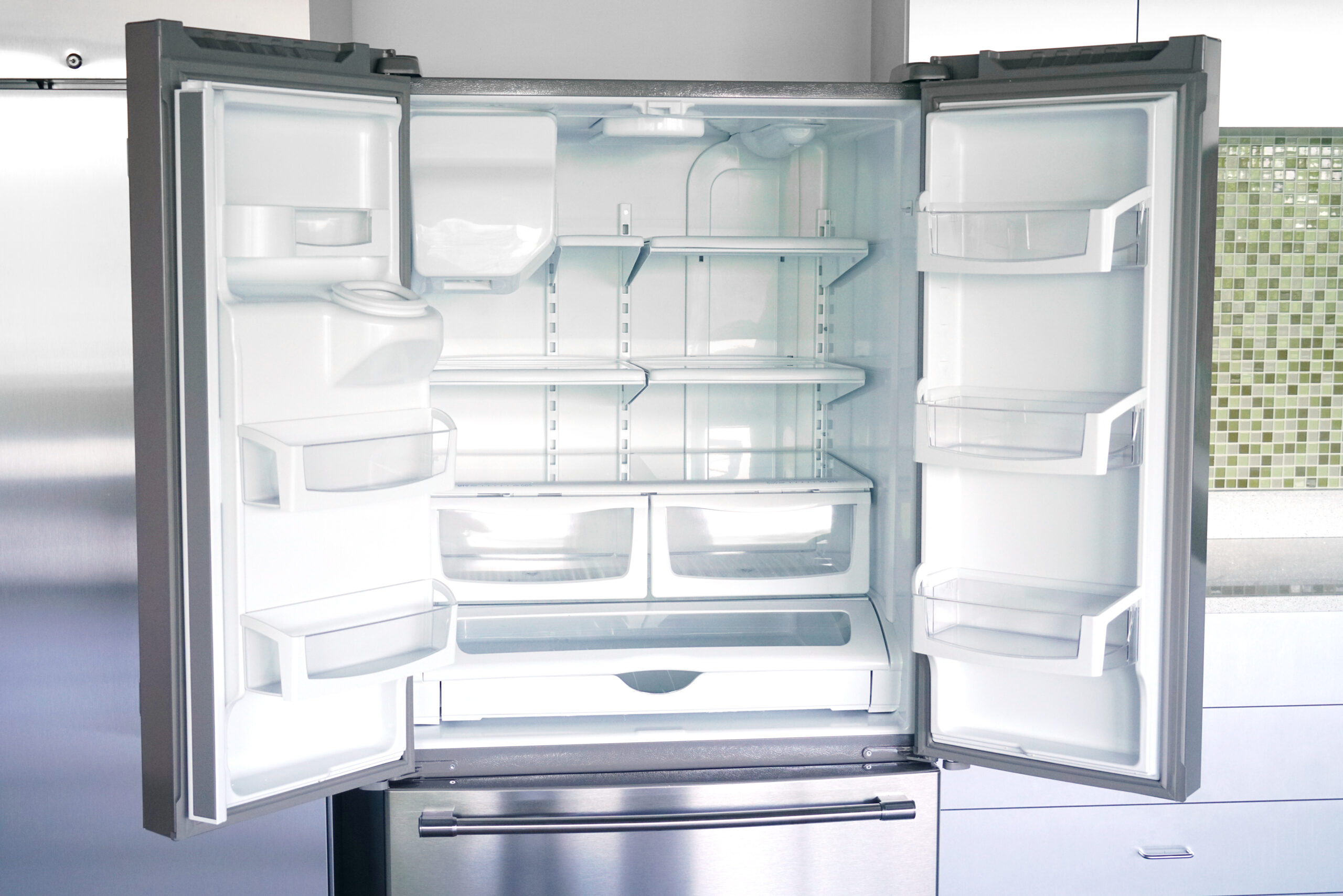Open stainless steel refrigerator with empty shelves and drawers, showing an empty interior and glass shelves
