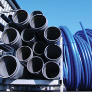 Stacked black metal pipes on a rack beside curled blue industrial hoses in an outdoor yard.
