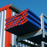 Blue pvc pipes with orange ends stacked on a metal rack at a construction site.