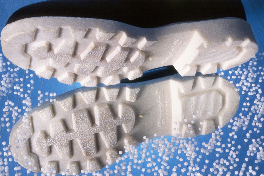 Shoes | Reedy Chemical Foam Bottom view of two white running shoe outsoles with rugged tread on a blue background with white beads/balls nearby, showing tread details and grip patterns.